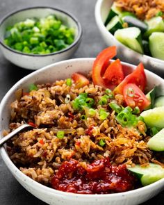 two bowls filled with rice and vegetables on top of a black table next to green onions