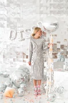 a woman in a silver dress standing next to a giant balloon and some confetti