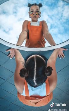 a woman in an orange top is looking at herself in the mirror with her hands behind her head