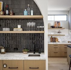 a kitchen with marble counter tops and wooden cabinets, along with wine glasses on the shelves