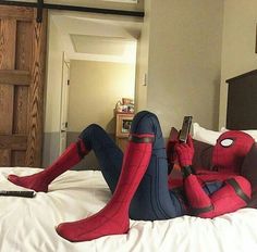 a spider man laying on top of a bed next to a remote control in his hand