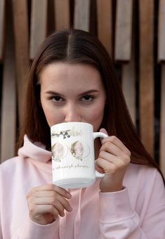 a woman wearing a pink hoodie is holding a coffee mug in front of her face