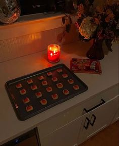 a lit candle sits on top of a cookie sheet next to some candy and flowers