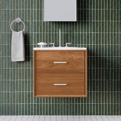 a bathroom with green tiled walls and a wooden sink vanity next to a white towel hanging on the wall