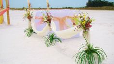 an outdoor ceremony set up on the beach with flowers in vases and hanging draping