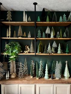 christmas trees are displayed on wooden shelves in a room with green walls and white cupboards