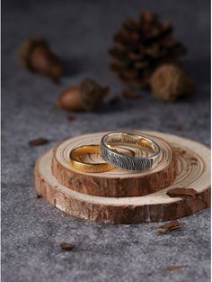 two wedding rings sitting on top of a piece of wood with pine cones in the background