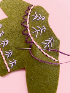 two pieces of green felt with white and pink thread on them