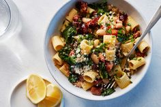 a white bowl filled with pasta and spinach next to lemon wedges on a table