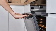 a person pulling something out of an oven with their hand on the door and in front of it