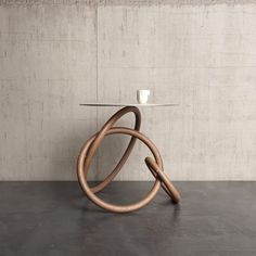 a wooden table with a glass top and two rings on the base, in front of a concrete wall