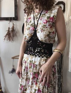 a woman standing in front of a white wall wearing a dress with flowers on it