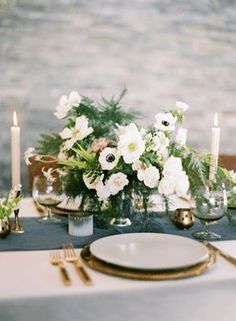 the table is set with white flowers and gold place settings, candles and napkins