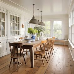 a dining room table with chairs and vases on it in front of two windows