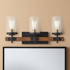 three light bathroom vanity fixture with wood and glass shades on the top, along with a mirror