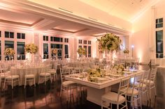 a room filled with lots of tables covered in white cloths and chairs next to tall windows