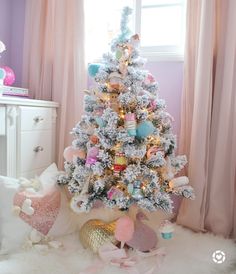 a white christmas tree with pink, blue and gold ornaments in a bedroom decorated for the holidays