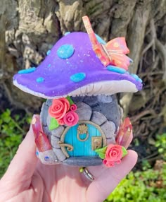 a purple mushroom with flowers and a house on it's side is held up in front of a tree