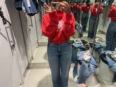 a woman taking a selfie in front of a mirror while wearing jeans and a red shirt