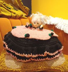 a crocheted doll sitting on top of a pillow in front of a yellow wall