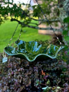 a green leaf shaped dish hanging from a chain in front of some bushes and trees