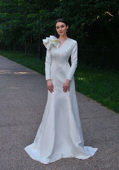 a woman in a white wedding dress standing on the sidewalk with her hands on her hips