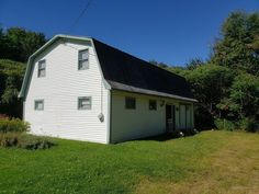 a small white building sitting on top of a lush green field in front of trees