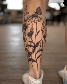 a woman's legs with flowers and butterflies tattooed on her lower leg, while she is wearing white tennis shoes