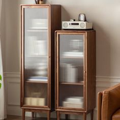 a tall wooden cabinet sitting next to a brown chair in front of a white wall