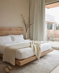 a bed with white sheets and pillows in a bedroom next to a large window that has sliding glass doors