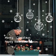 a man sitting at a table in front of a window decorated with christmas balls and ornaments