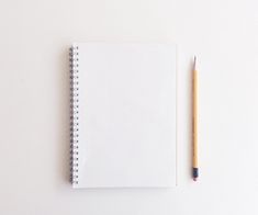 a notebook with a pencil next to it on top of a white surface, against a plain background