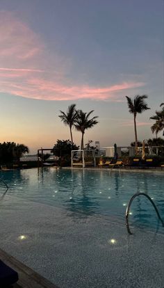 an empty swimming pool with palm trees and the sun setting in the distance behind it