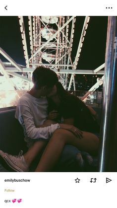 a man and woman sitting next to each other in front of a ferris wheel at night