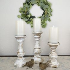 three candles are sitting on a table with two birds next to them and a wreath