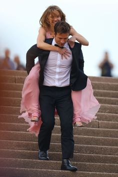 a man in a tuxedo carrying a woman on his back down some steps