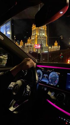 a man driving a car at night in front of a large building with gold and red lights