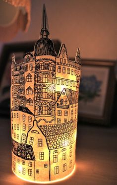 a lit candle holder with buildings drawn on it