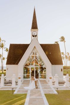 a bride and groom standing in front of a white church with palm trees behind them