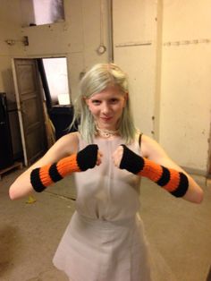 a woman in a white dress is holding her hands up with two black and orange knitted gloves