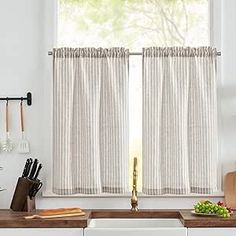 a kitchen with a sink, counter and window covered in white curtained drapes