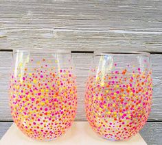 two hand painted wine glasses sitting on top of a wooden table next to each other