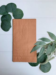 a book and some green leaves on a white table with a wooden frame in the middle