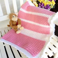 a stuffed monkey sitting on top of a pink and white crocheted blanket next to flowers