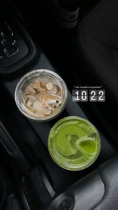 two plastic cups filled with green liquid sitting on top of a car dash board next to a cup holder