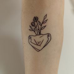 a small tattoo on the leg of a woman with flowers in her heart shaped vase