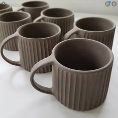 four coffee mugs are lined up on a white counter top, with the handles slightly down