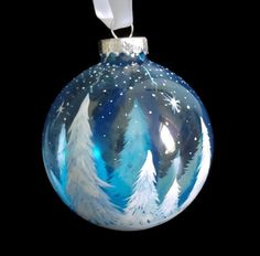 a glass ornament with trees and snow on the top, hanging from a white ribbon