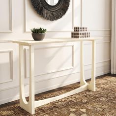 a white table with a plant on it in front of a mirror and wall hanging