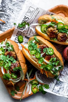 three meatball subs with green peppers and onions on a wooden tray next to an apple